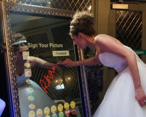 Bride using a magic mirror photo booth to sign her picture at a wedding